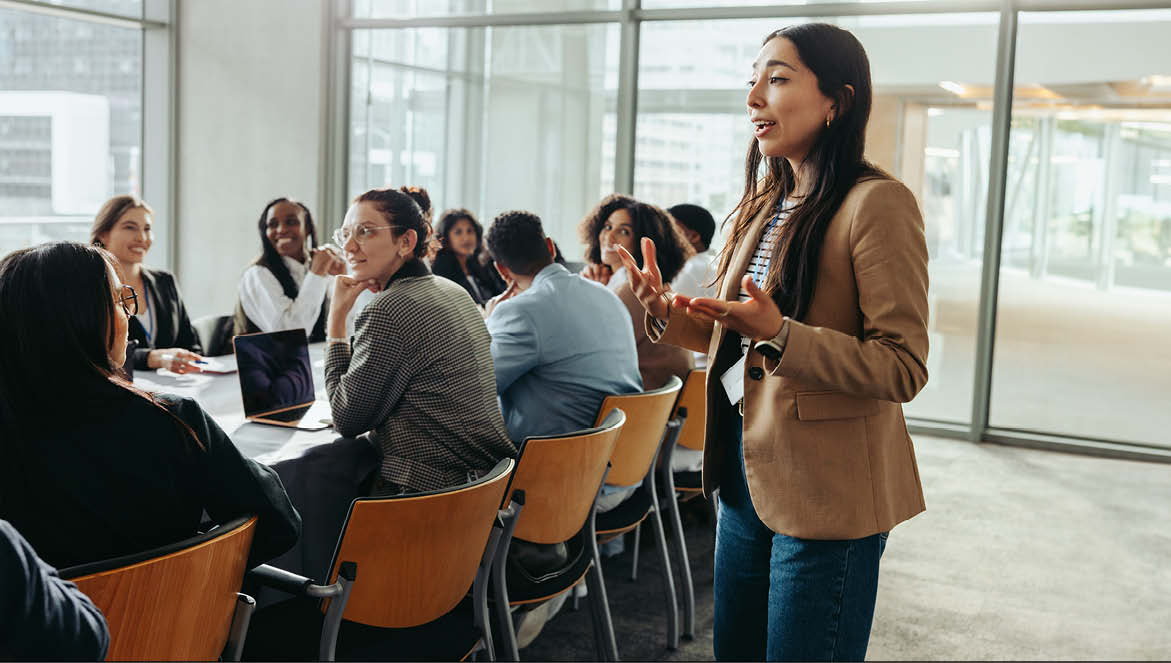 A group of young people sat around a table listening to someone talk
