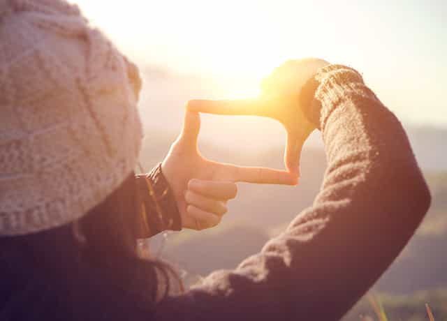 An image of a woman holding up her fingers and looking through them at a distant landscape