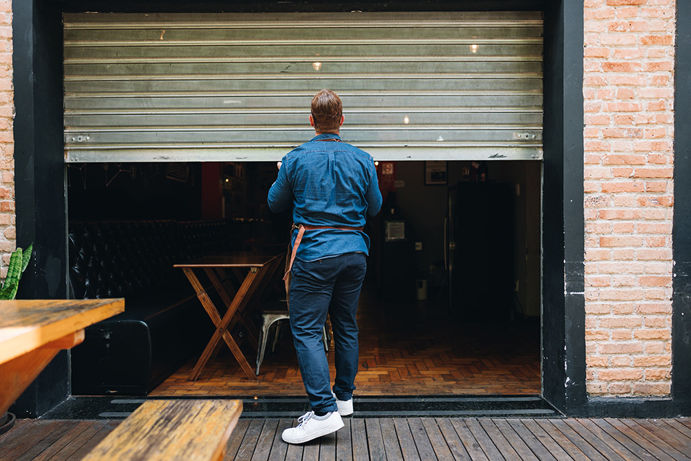 Man outside retail premises in blue denim, closing shop shutters he could be considering small business rates relief