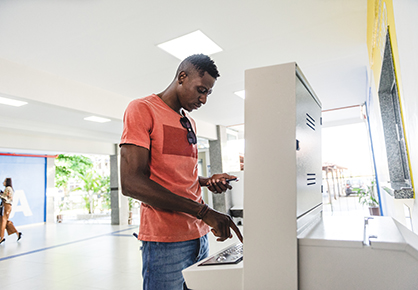 Man stood beside machine registering attendance in public sector building on a computer