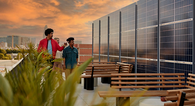 Three people walking on the roof of a office building looking at solar panels